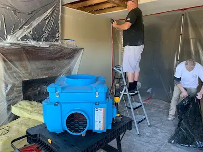 Plastic containment, an air scrubber and a crew opening a wall during structural drying