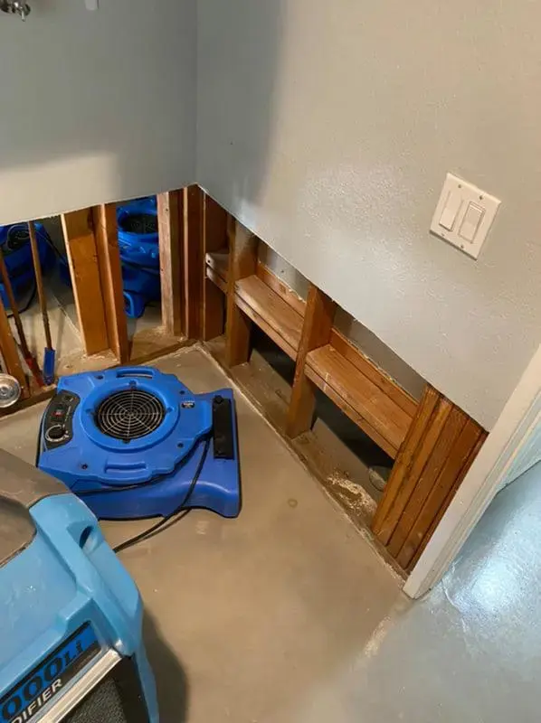 Air movers aimed at an opened cabinet base to dry the wet cavity behind it