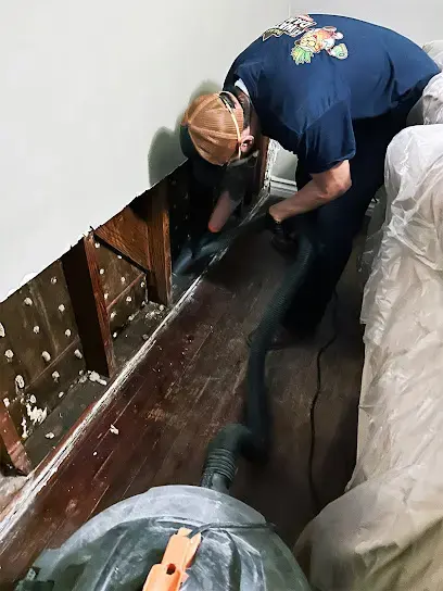 A technician cutting out a wet wall bottom behind plastic sheeting