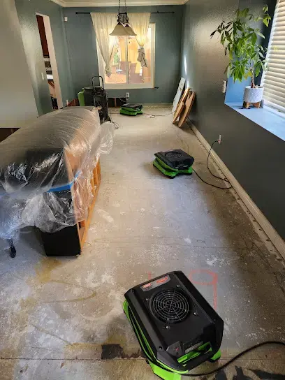 Air scrubber and plastic sheeting set up along a long room during water damage restoration in Colton