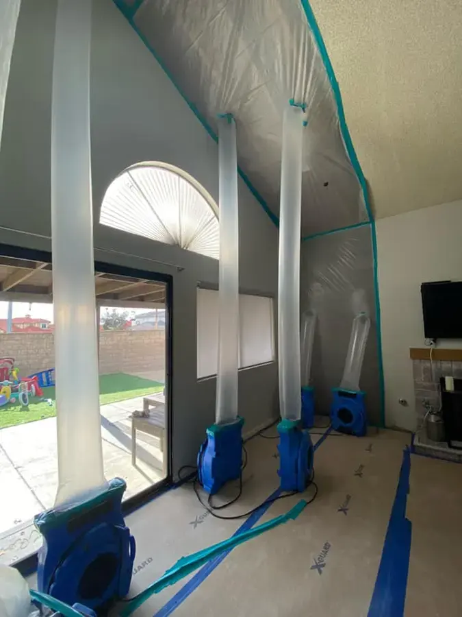 Air movers and a dehumidifier drying a living room after flooring was lifted over a slab leak