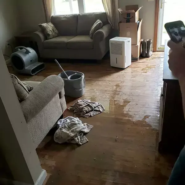An air mover blowing across a wet living room floor in a Colton house, drying it until readings settle